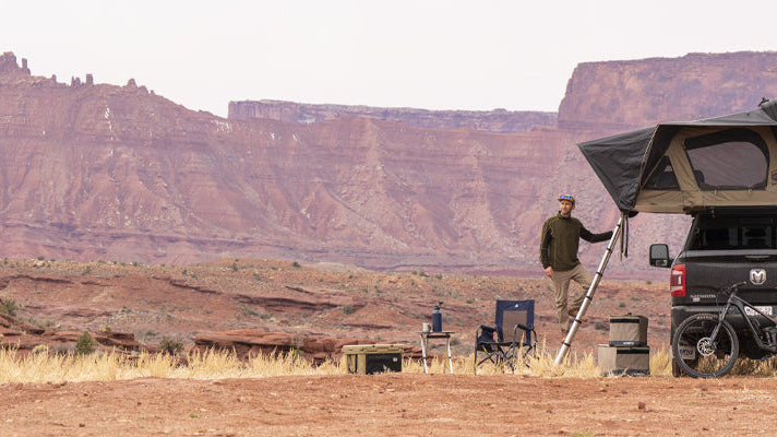 A man standing on a ladder attached to a CVT setup above a Dodge Ram pickup truck in the desert.