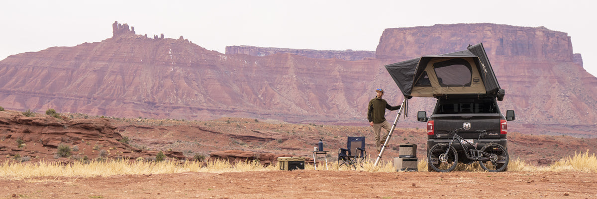 A man standing on a ladder attached to a CVT setup above a Dodge Ram pickup truck in the desert.